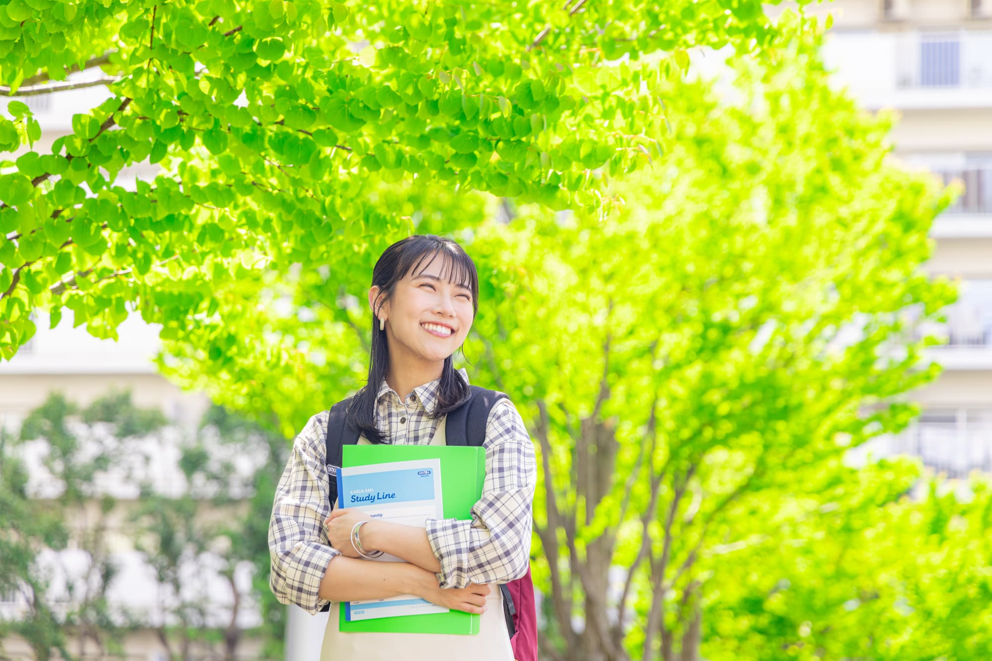 新緑の中で勉強道具を抱え微笑む女性