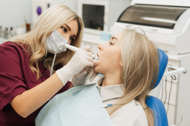 女性歯科医師が機器を使って女性の歯石取りをしている