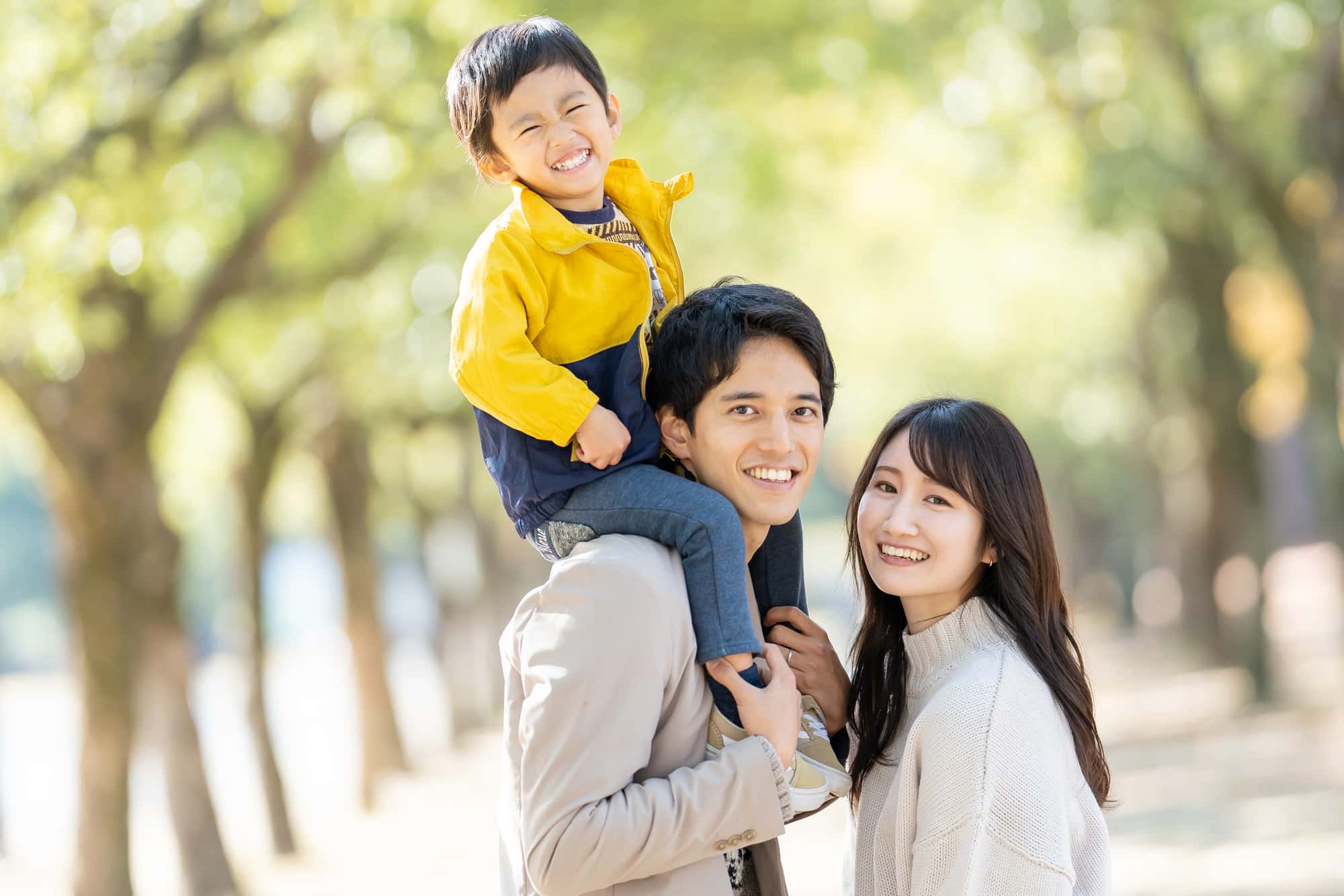 肩車されて笑顔の子どもと両親が散歩しているイメージ