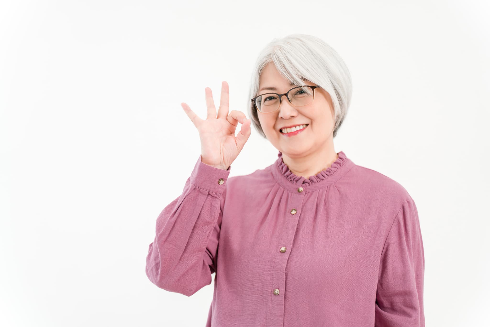 健康なのでインプラント治療は受けられると手でOKサインをするシニア女性